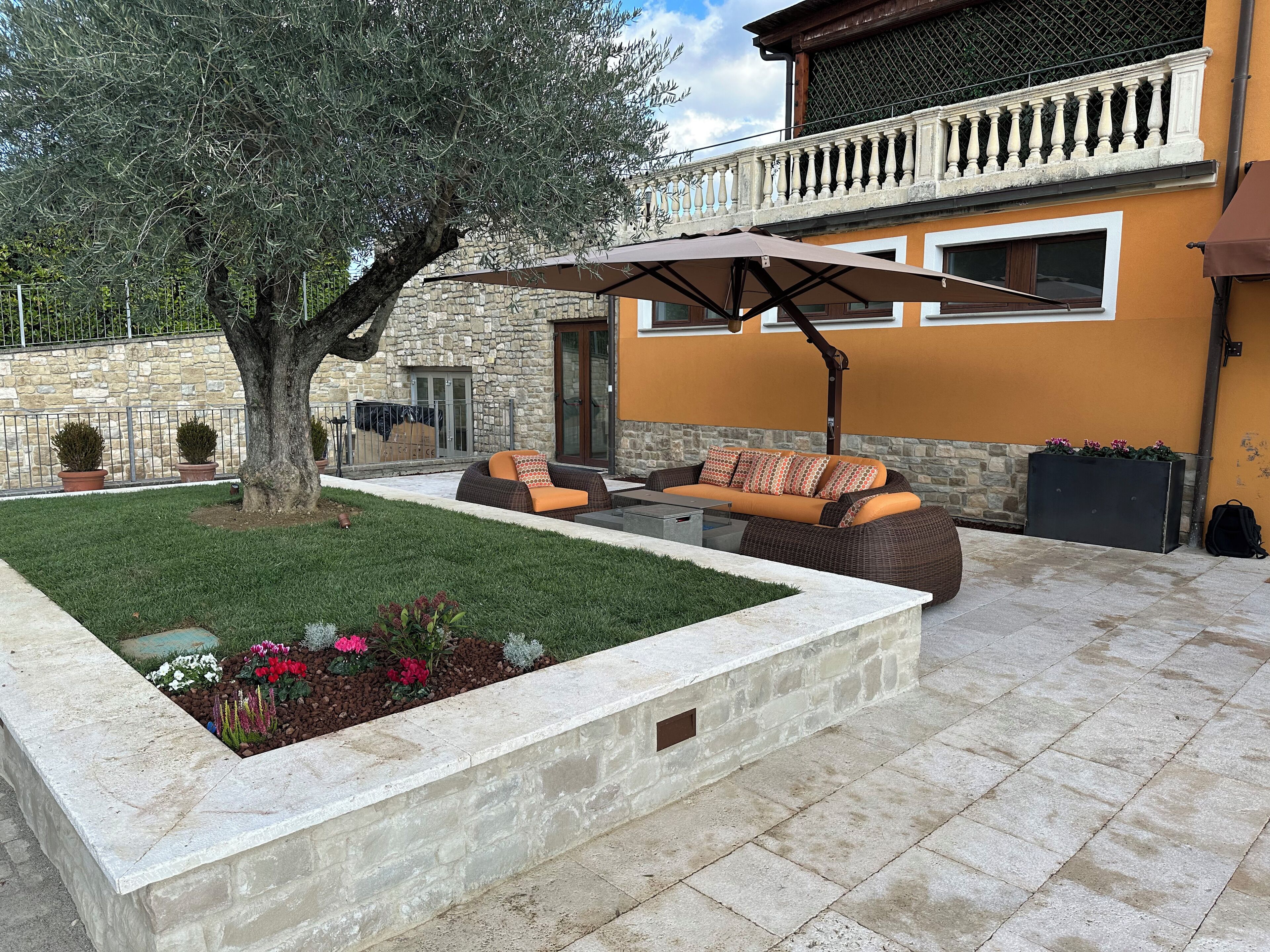 Eine Terrasse mit Gartenmöbeln, einem Baum und einer Steinmauer.