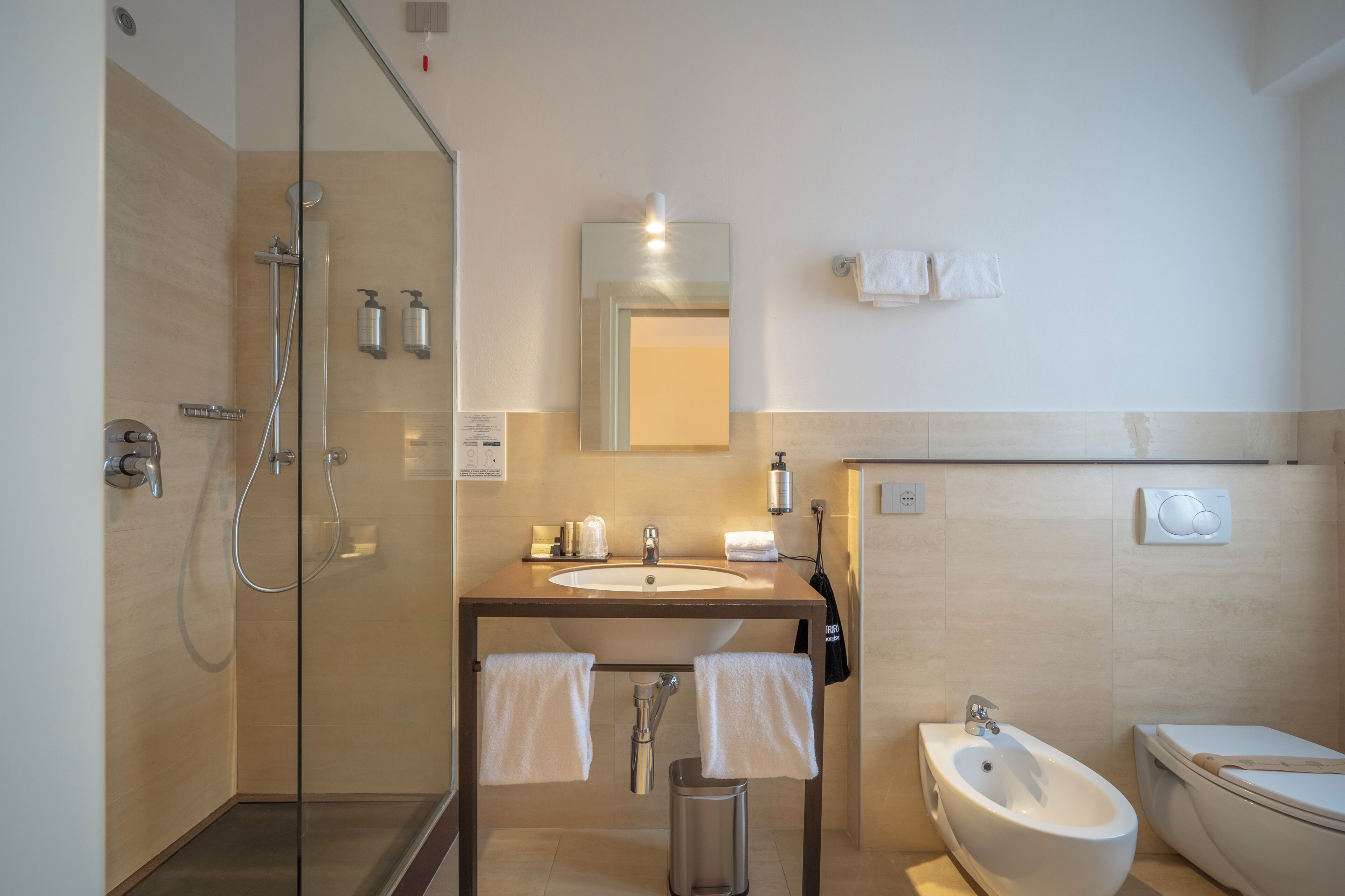 A modern bathroom with a glass-enclosed shower, a sink with a mirror above, a bidet, and a toilet.