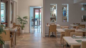 A modern dining area with multiple tables and chairs, potted plants, and a view of the outdoors.