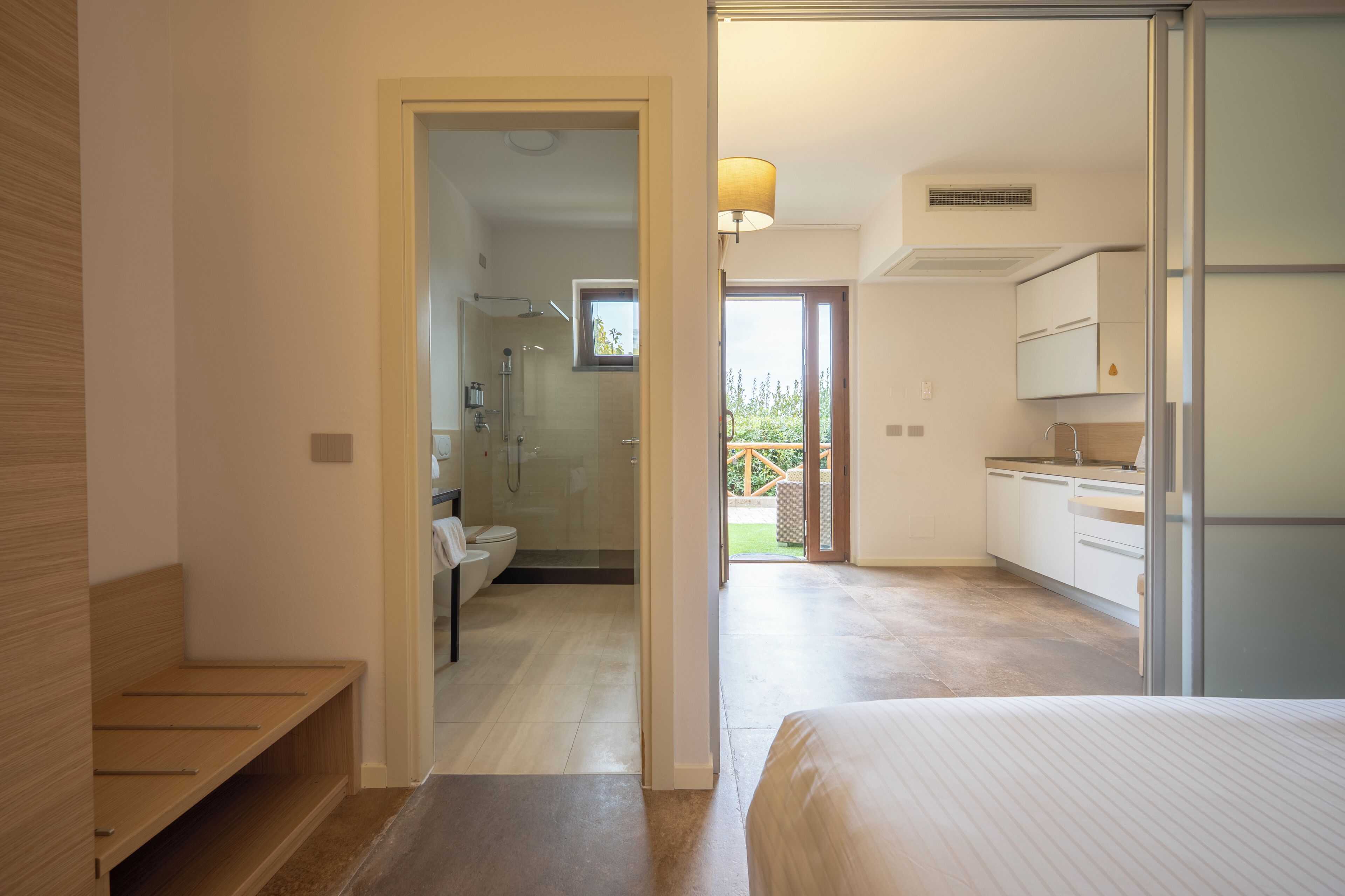 A modern bedroom with a large bed, a bathroom with a shower, and a kitchen area.