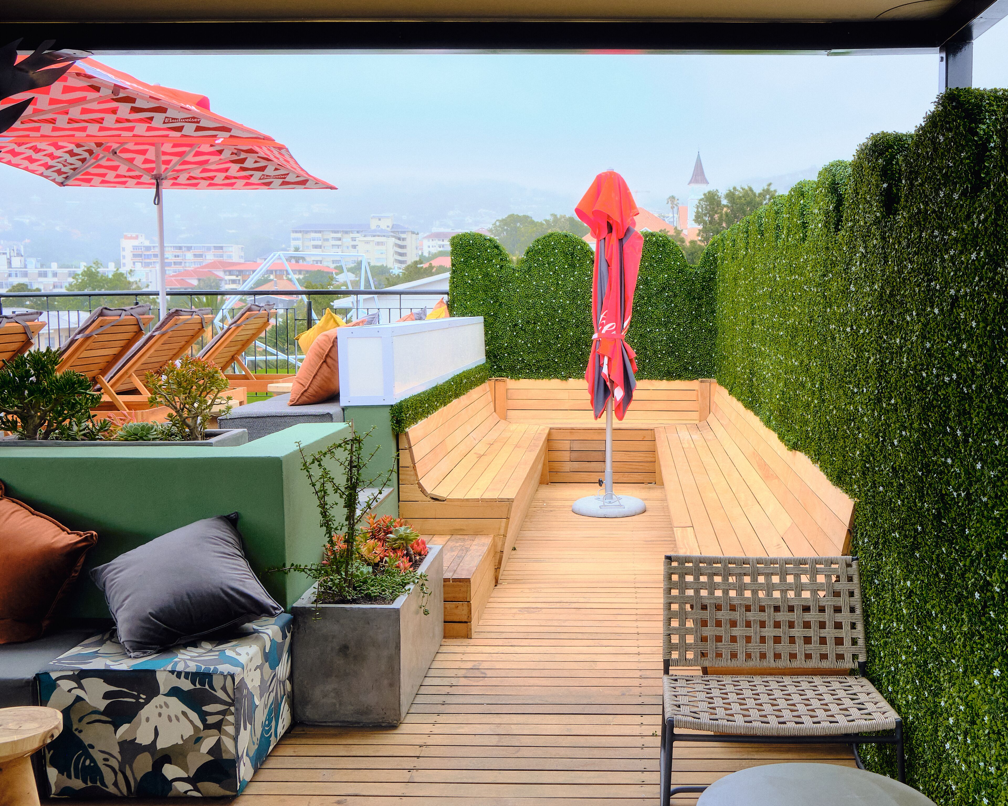 Una terrazza sul tetto con sedute in legno, un ombrellone rosso e vista sulla città.