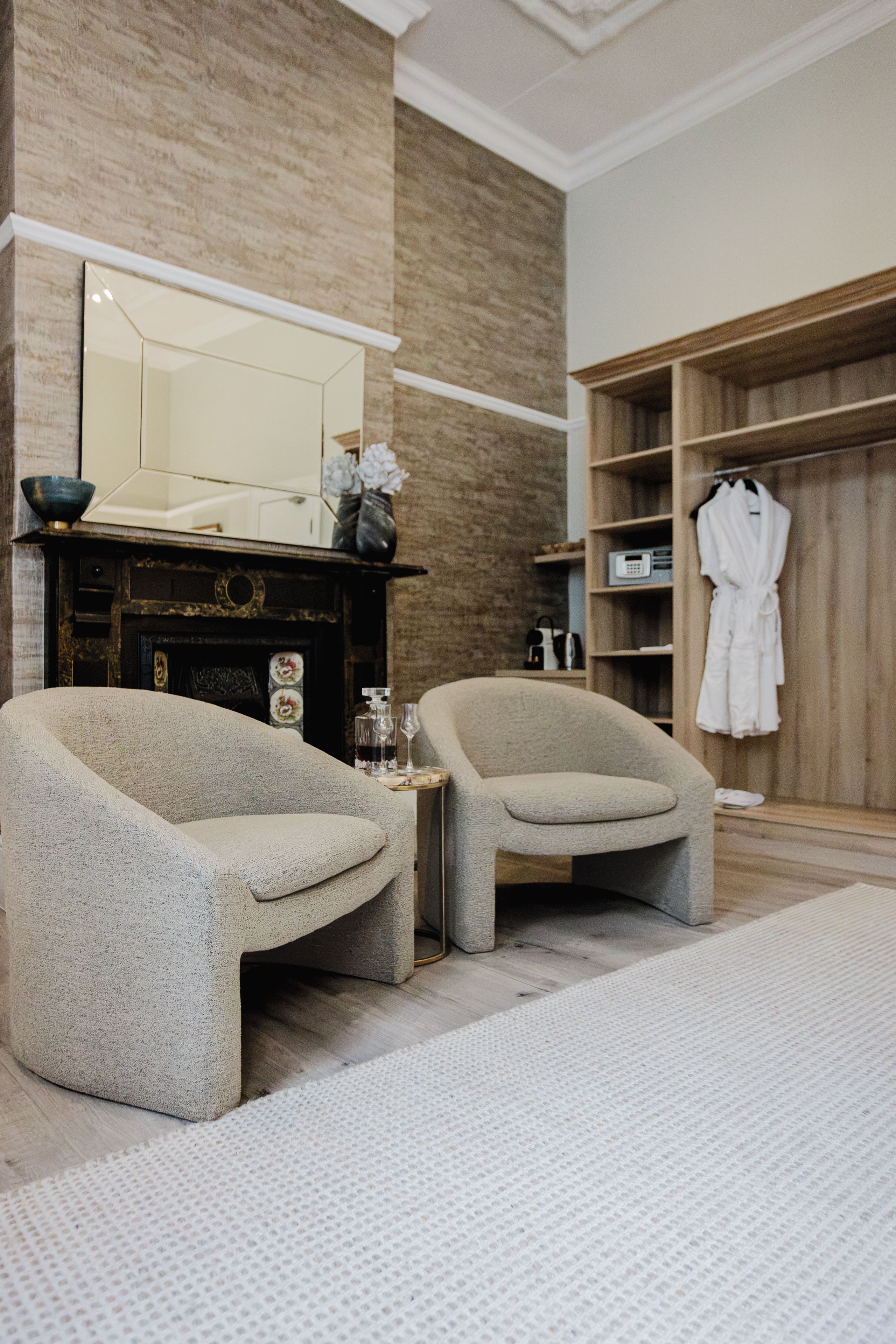 A modern bathroom with two armchairs, a mirror, and a robe rack.
