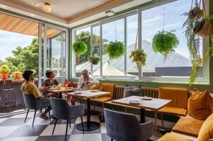 A modern cafe with large windows, indoor plants, and a checkered floor.