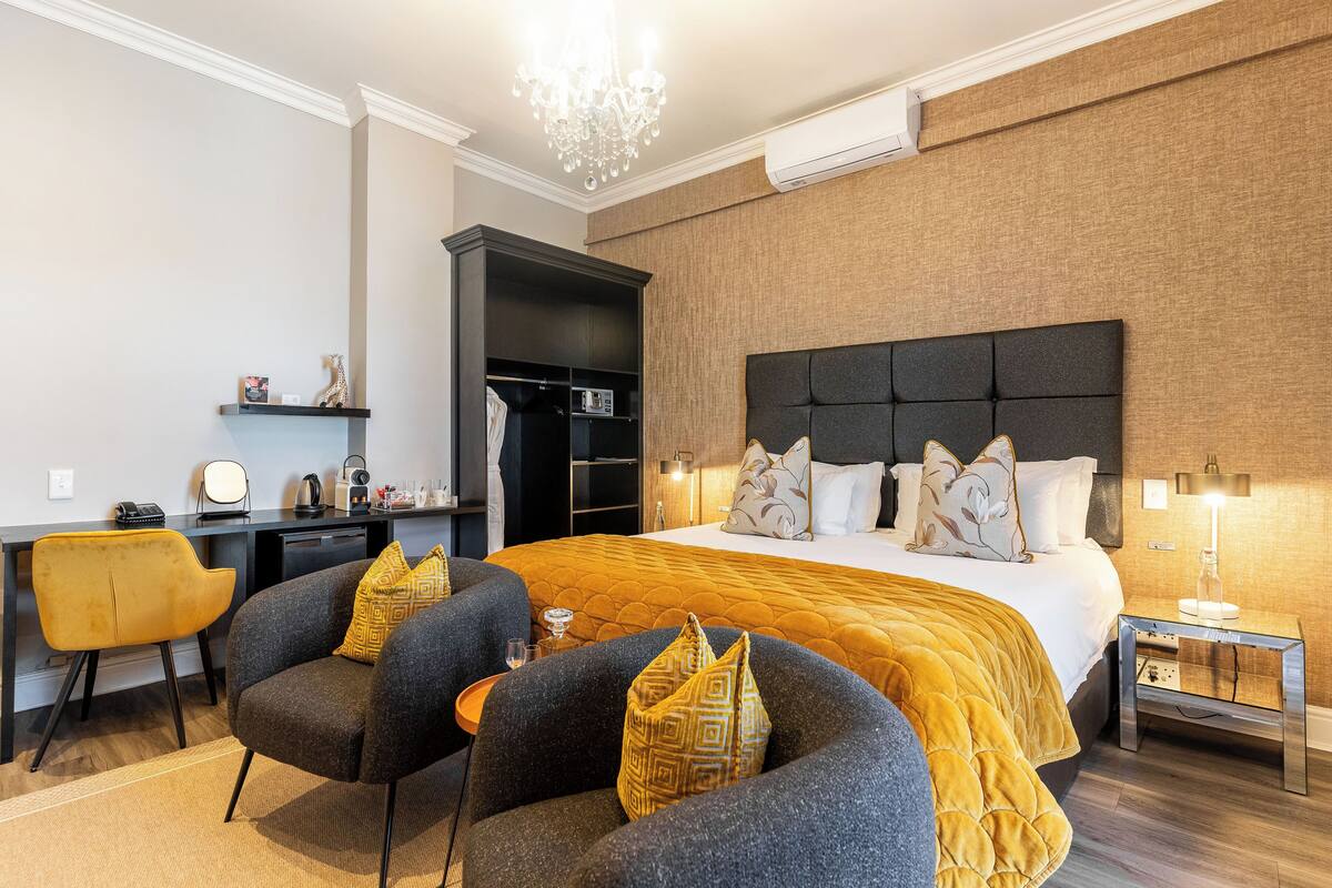 A hotel room with a large bed, a desk, a wardrobe, and a chandelier.