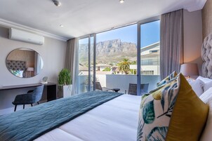 A hotel room with a large bed, a desk, a chair, a round mirror, and a view of a mountain.