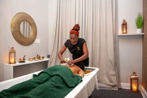 A massage therapy room with a massage table, a large mirror, and a shelf with candles and a plant.
