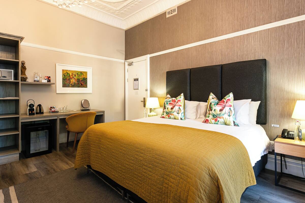 A hotel room with a bed, desk, chair, and a small refrigerator.
