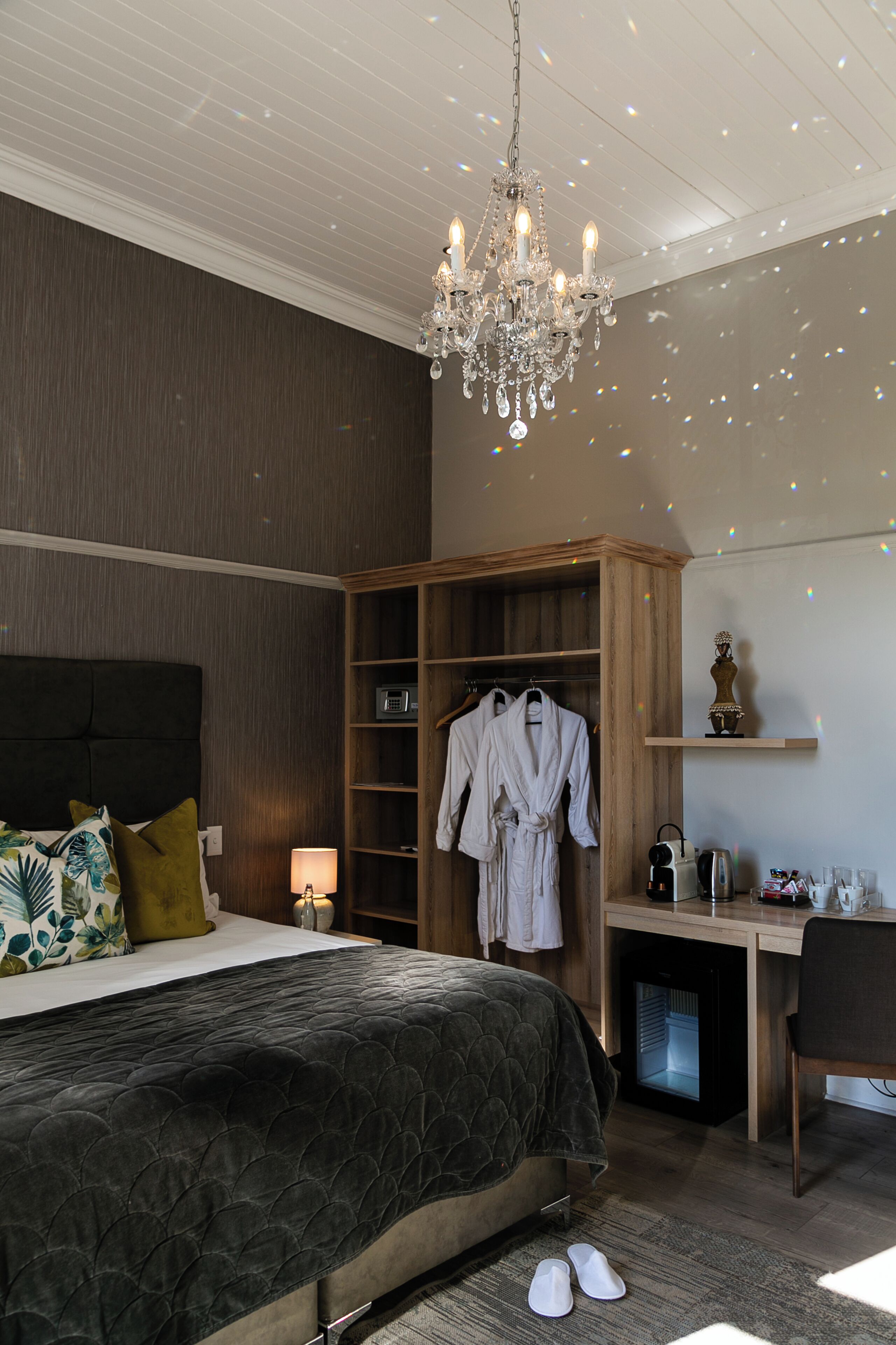 A bedroom with a bed, a wardrobe, a desk, and a chandelier.