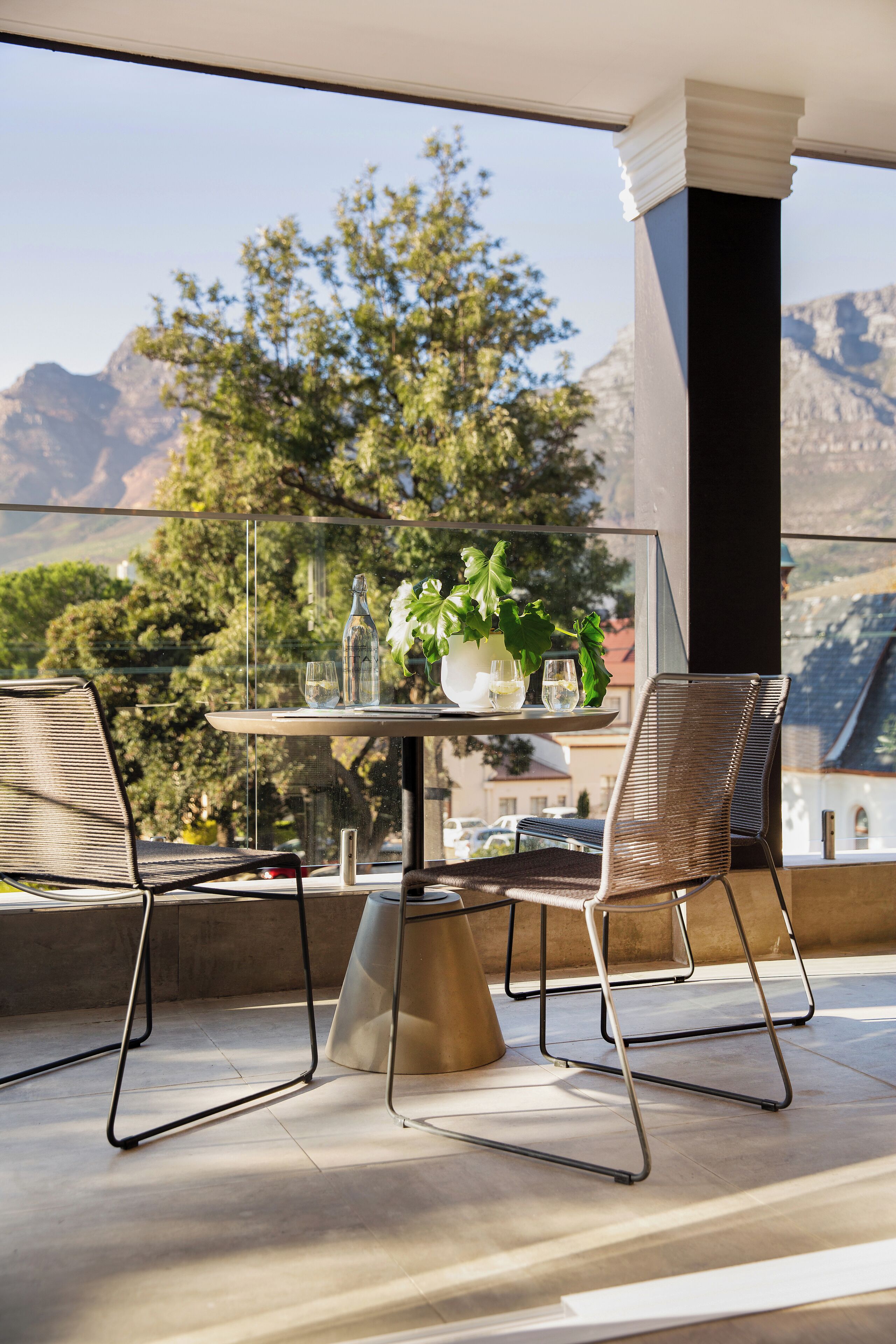 A balcony with a table set for two, featuring a bottle, glasses, and a potted plant.