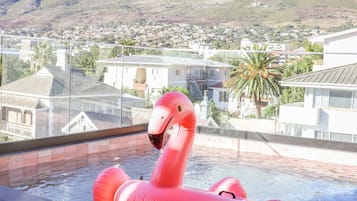 A hot tub with a pink flamingo float, overlooking a residential area with houses and a mountain in the background.