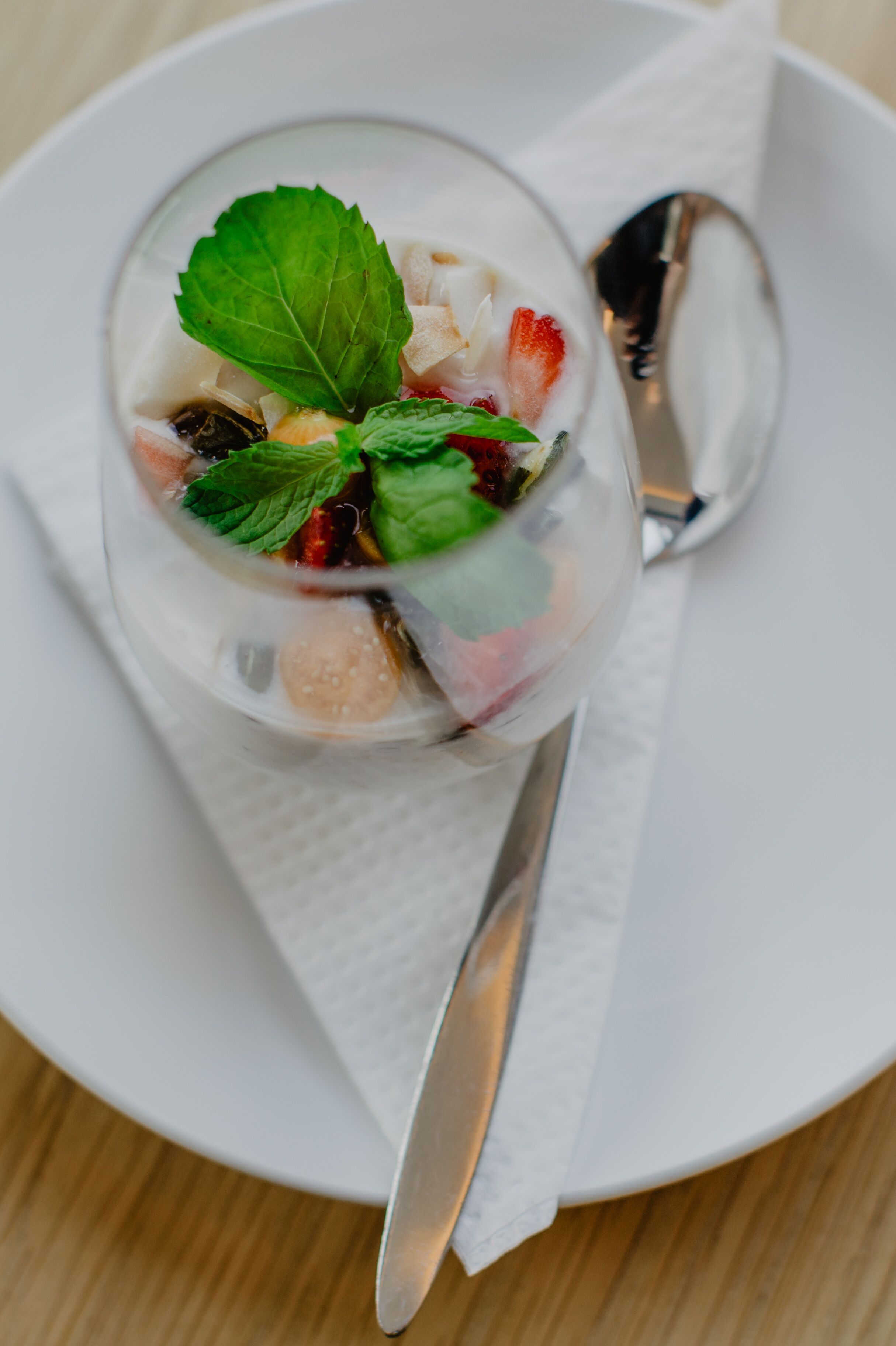 A dessert in a clear glass on a white plate with a spoon.