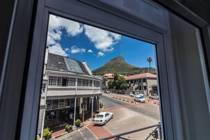 A view from a window of a street with buildings, a mountain, and cars.