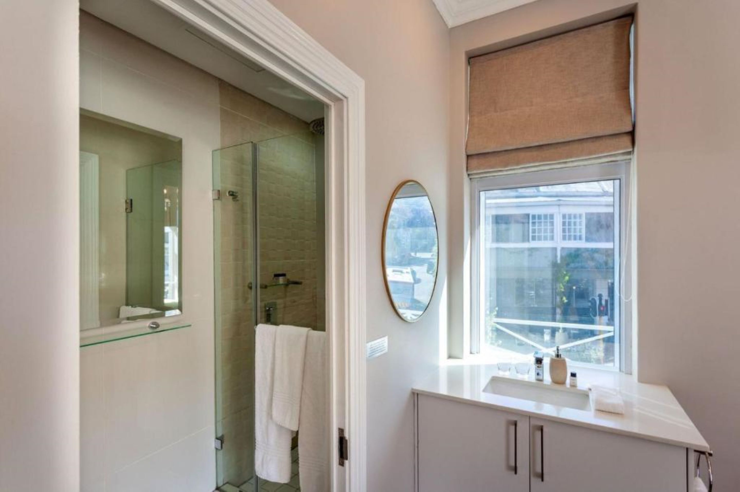 A modern bathroom with a glass shower enclosure, a large mirror, a vanity with a sink, and a window with a view.