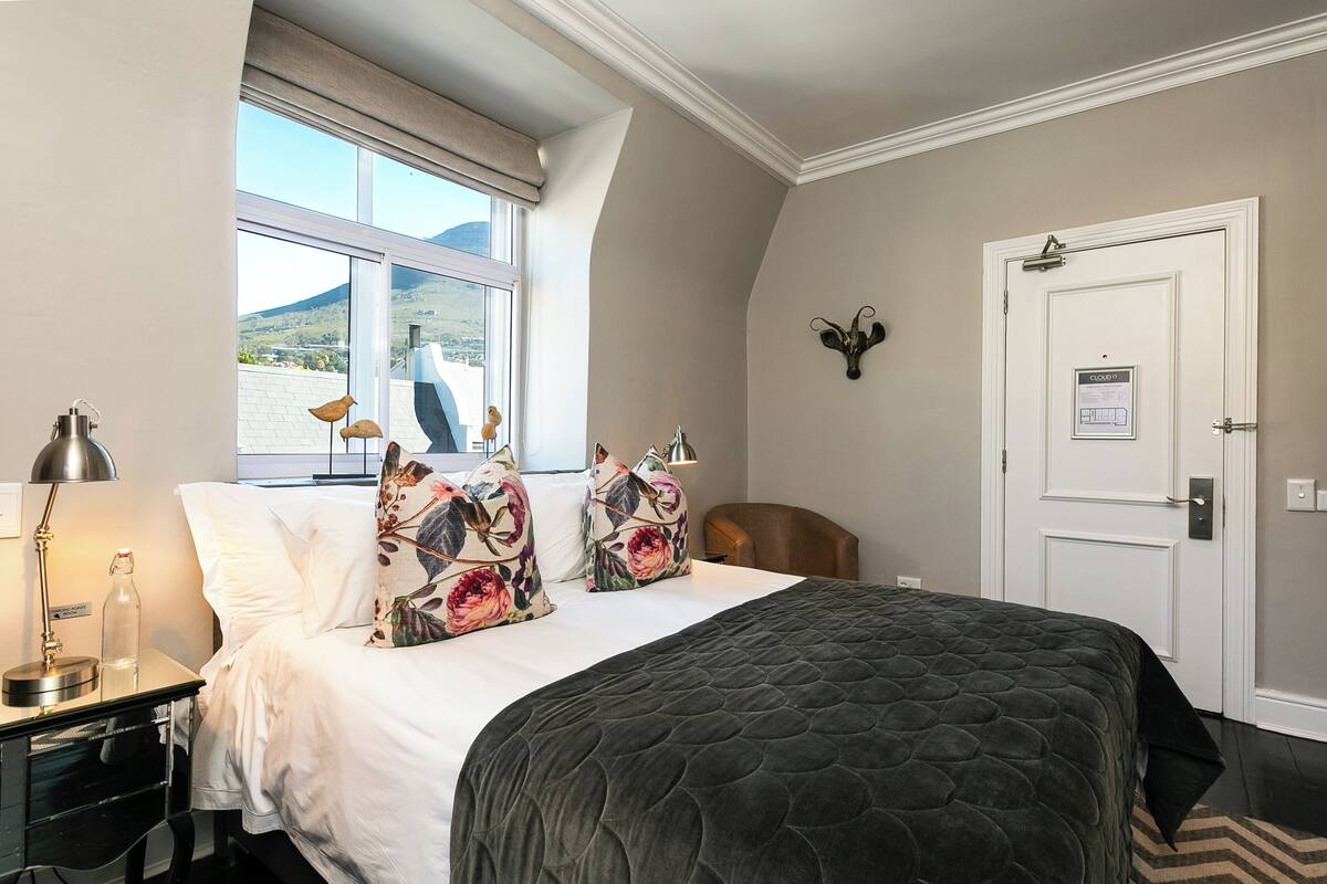 A bedroom with a bed, a nightstand, a lamp, a window with a view, and a door with a lock.