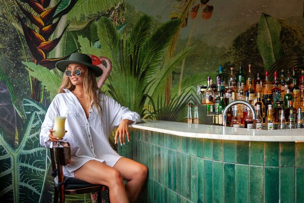 Una persona sentada en la barra con un mural tropical de fondo.