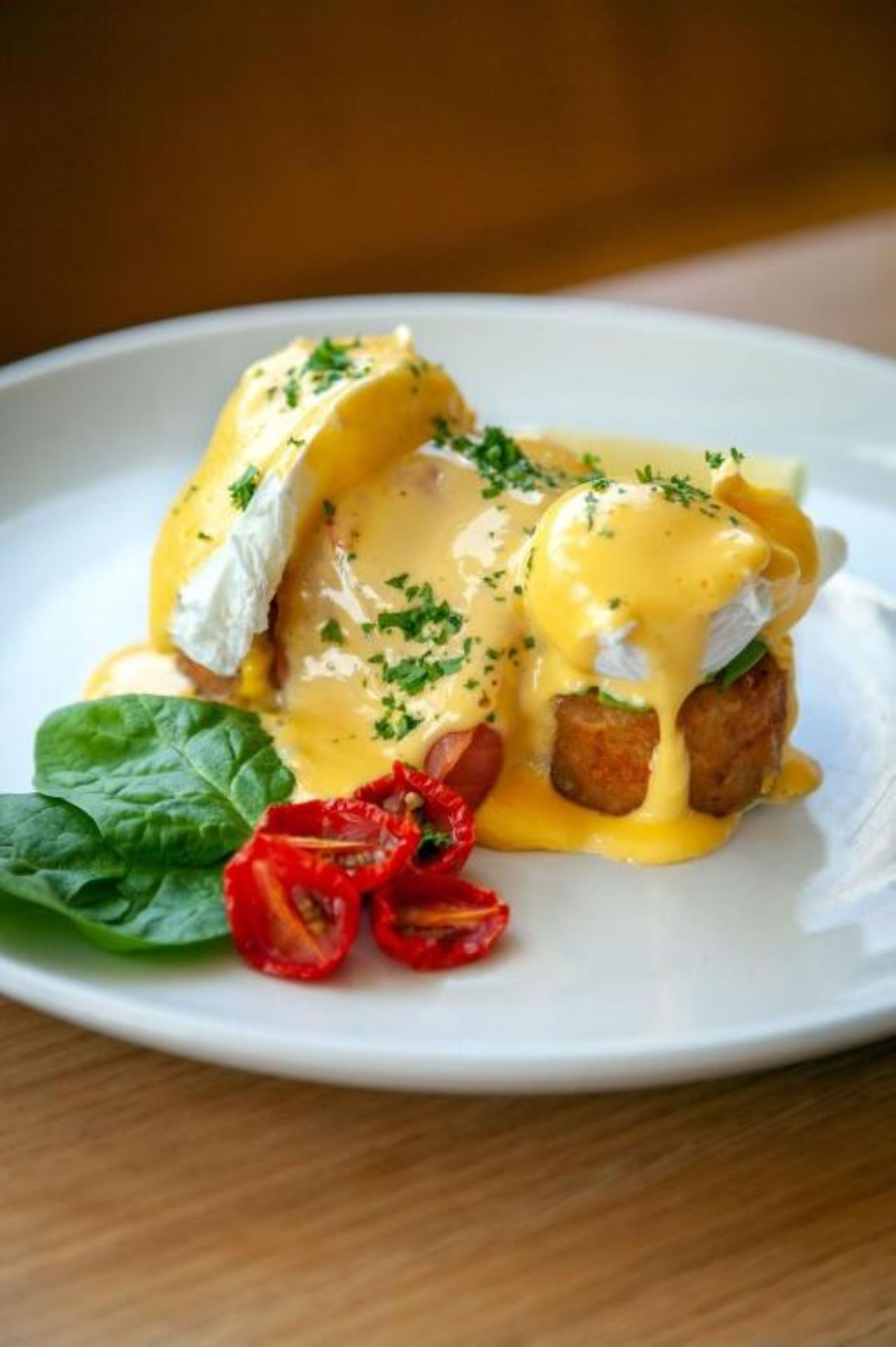 A plate with eggs benedict, hollandaise sauce, and garnishes.
