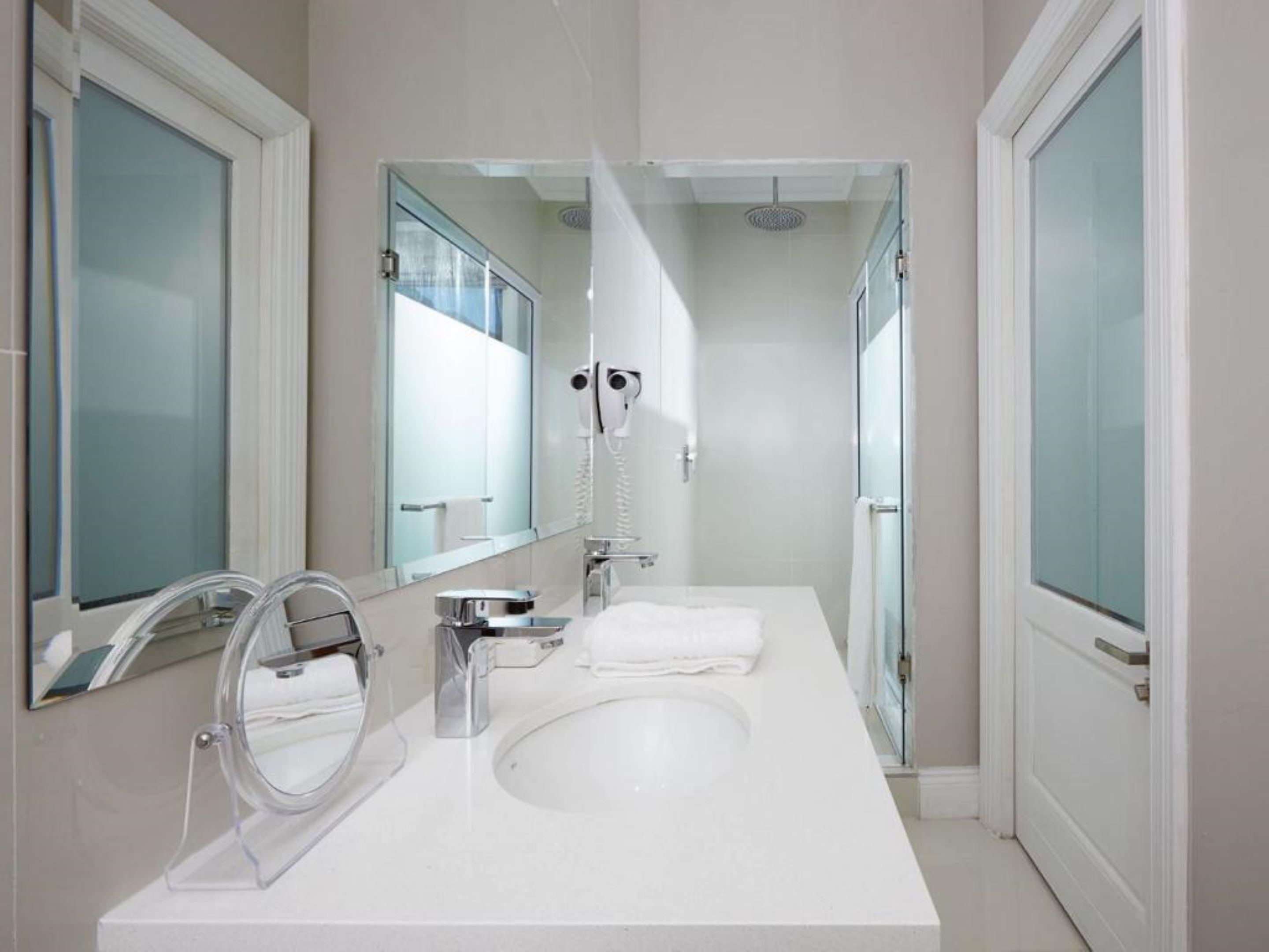 A modern bathroom with a large mirror, a sink, and a shower.