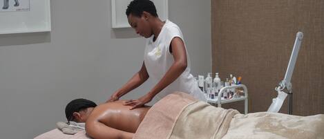 Une personne reçoit un massage du dos dans un spa, avec une table de massage, des serviettes et divers produits de spa en arrière-plan.