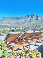 A rooftop lounge with wooden loungers and a view of a mountainous landscape.