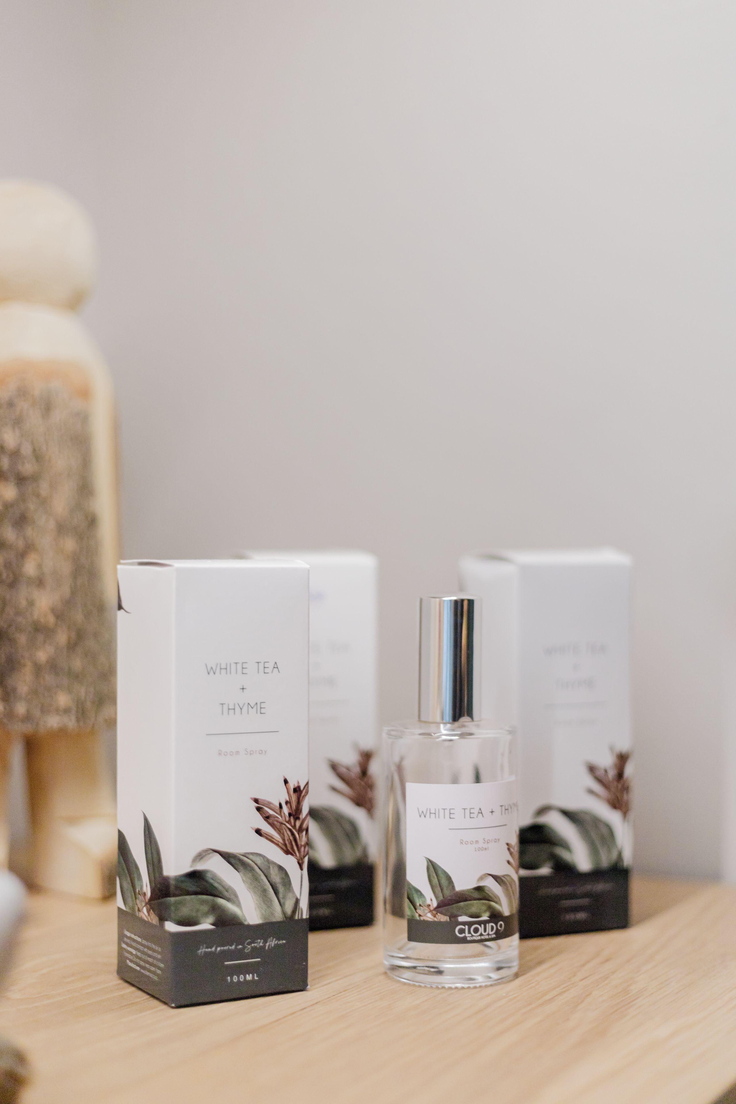 A set of white tea and thyme room spray bottles and boxes on a wooden surface.