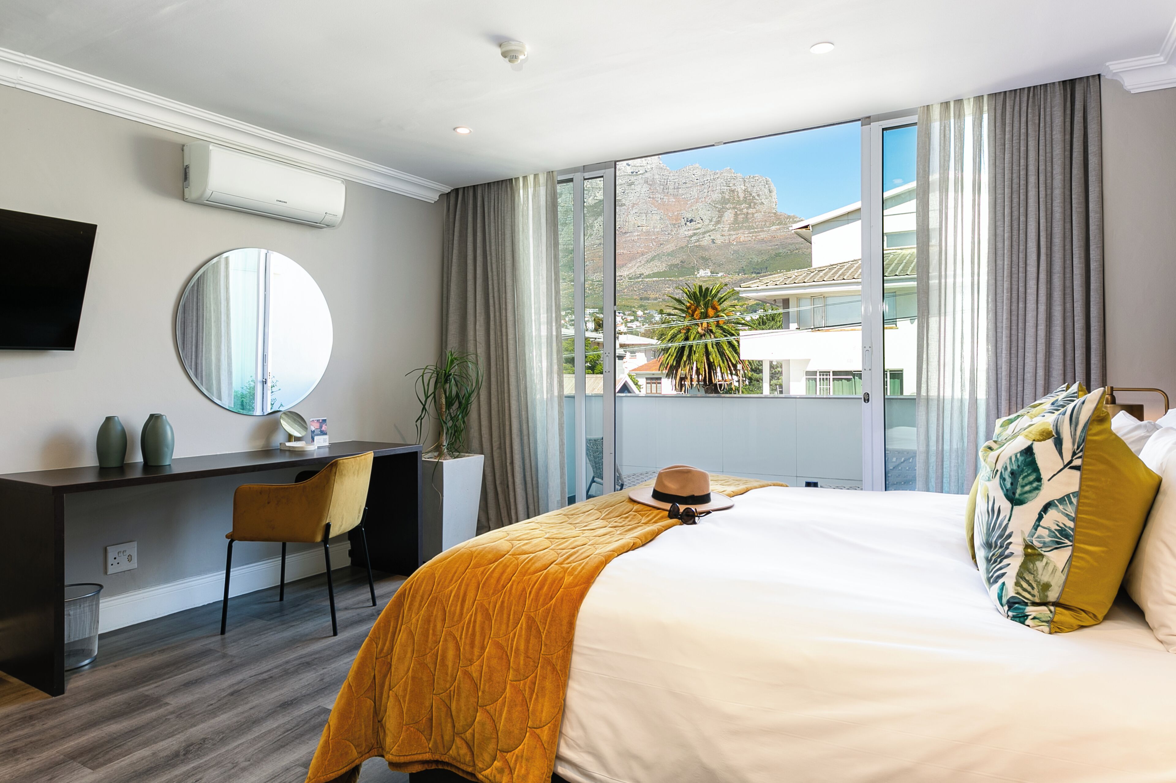 A hotel room with a bed, a desk, a chair, a TV, and a large window with a view of a mountain.