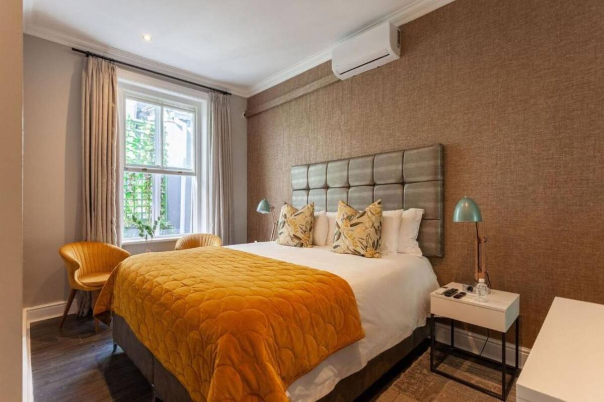 A hotel room with a large bed, a chair, a bedside table with a lamp, and a window with curtains.
