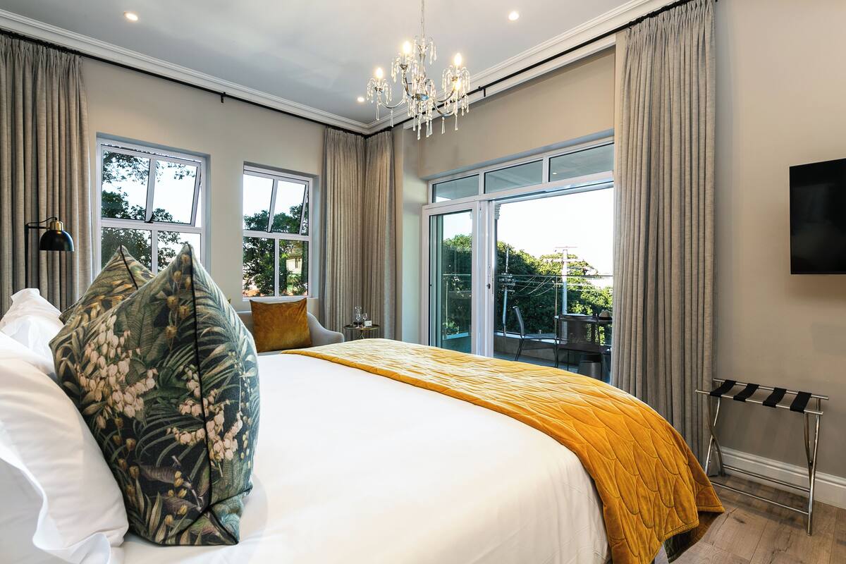 A hotel room with a large bed, a chandelier, a TV, and a balcony with a view.