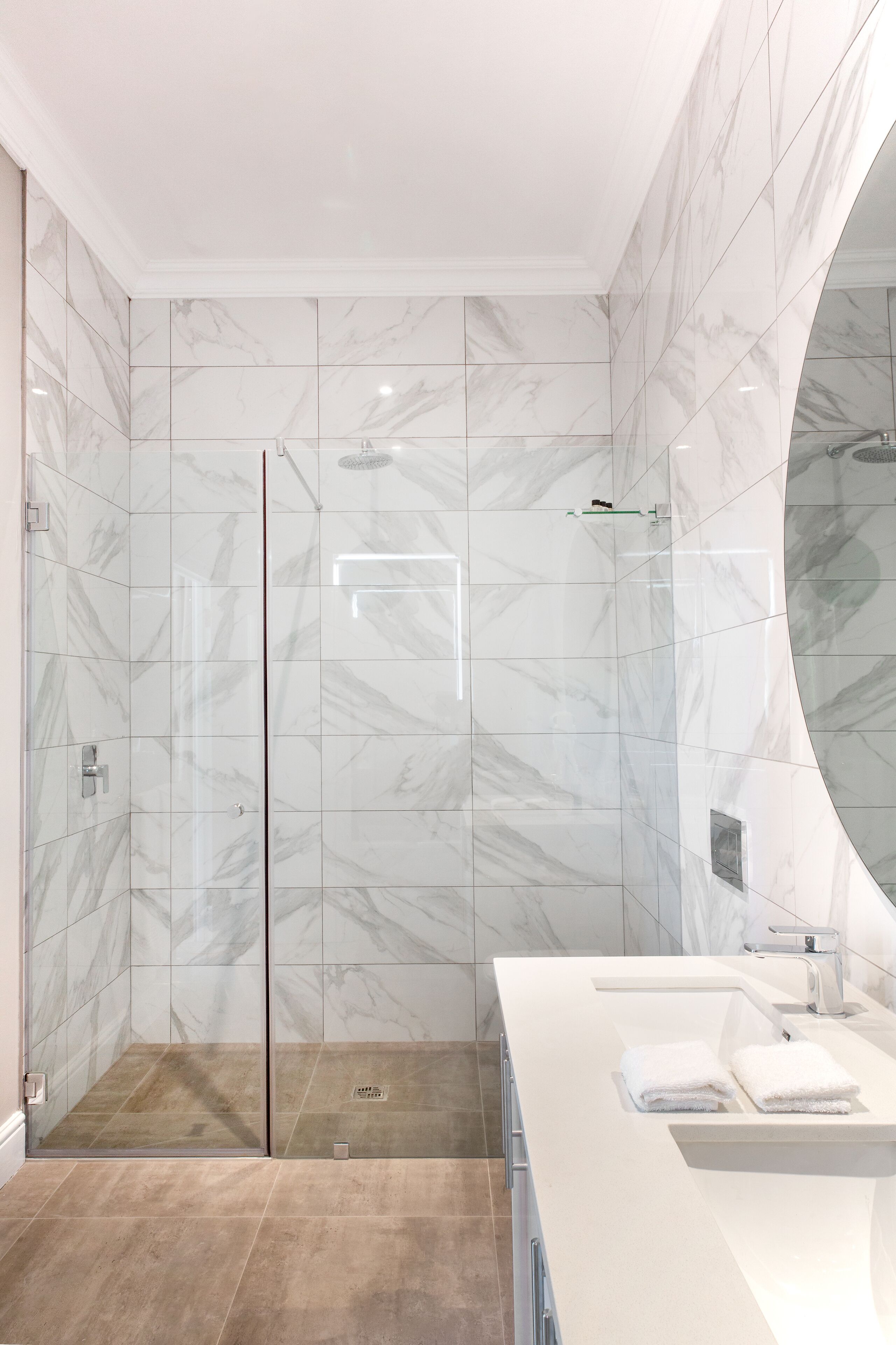 A modern bathroom with a glass-enclosed shower, a white vanity with a mirror, and marble-patterned walls.