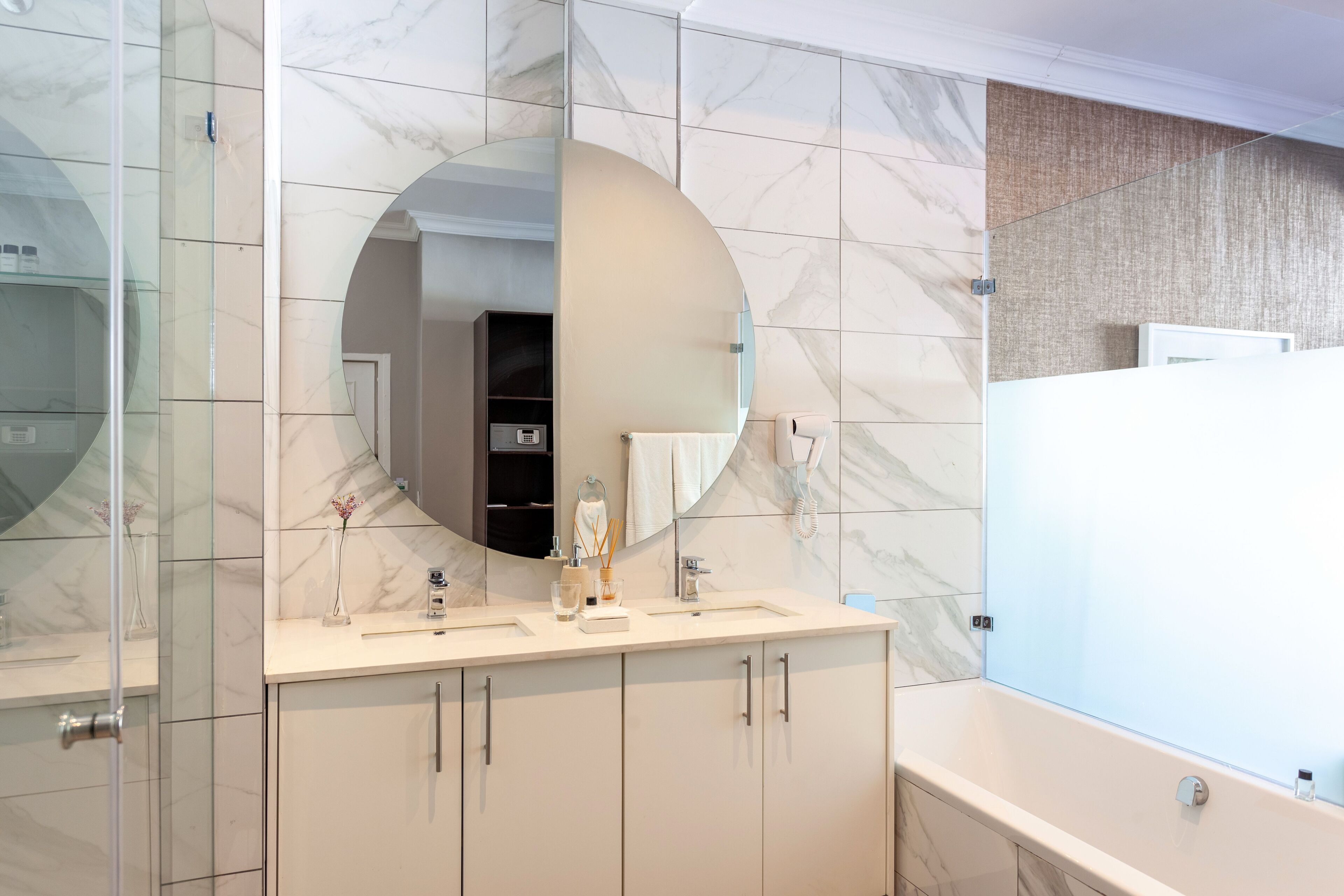 Une salle de bain moderne avec un pare-baignoire en marbre, un grand miroir, un lavabo avec une serviette et une baignoire.