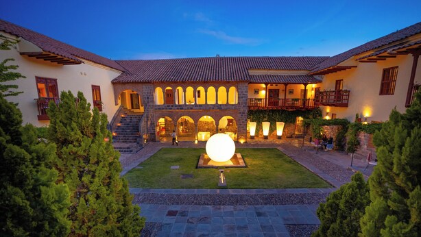 A courtyard with a large spherical sculpture, stone steps, and a building with arched windows and balconies. - Casa Cartagena Boutique Hotel & Spa (Cusco)