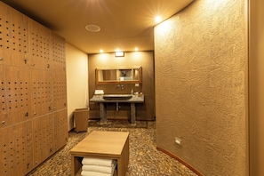 A bathroom with a wooden locker area, a sink with a mirror, and a small table with a towel.