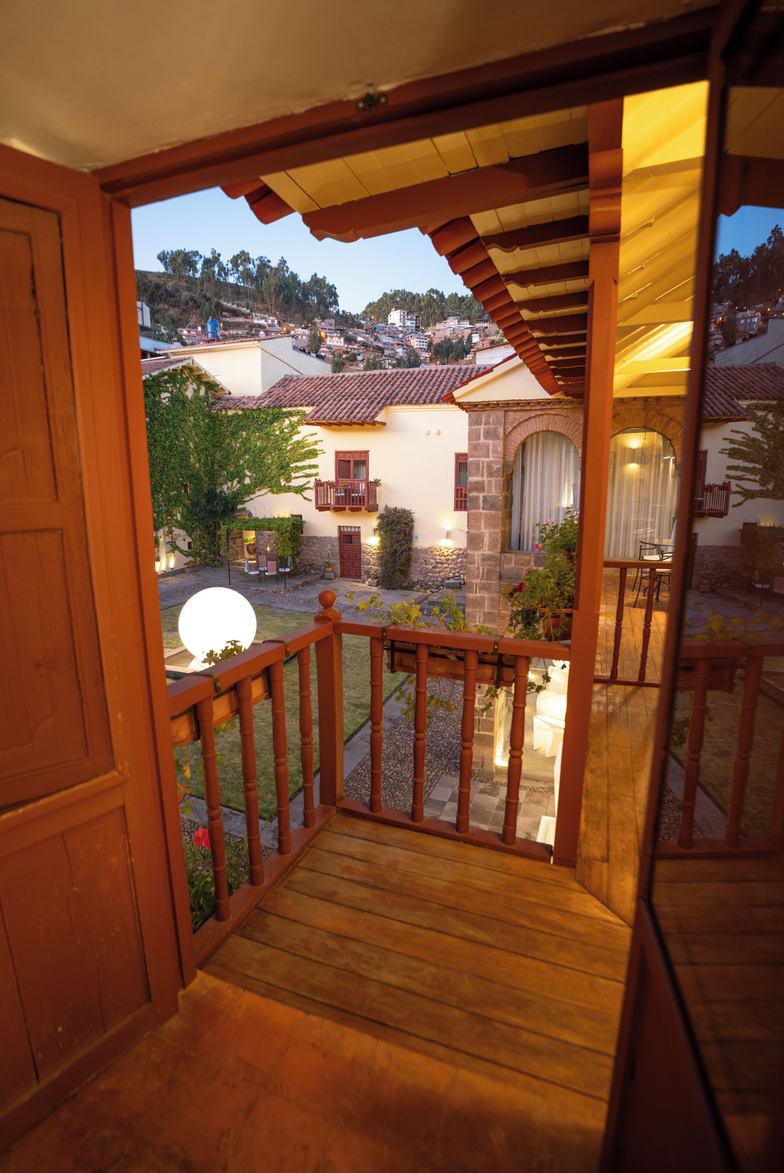 Un balcone in legno con vista su una zona residenziale, tra case e una collina.