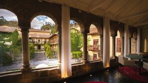 A spacious interior with stone columns, a red carpet, and a view of a courtyard with buildings and greenery. - Casa Cartagena Boutique Hotel & Spa (Cusco)