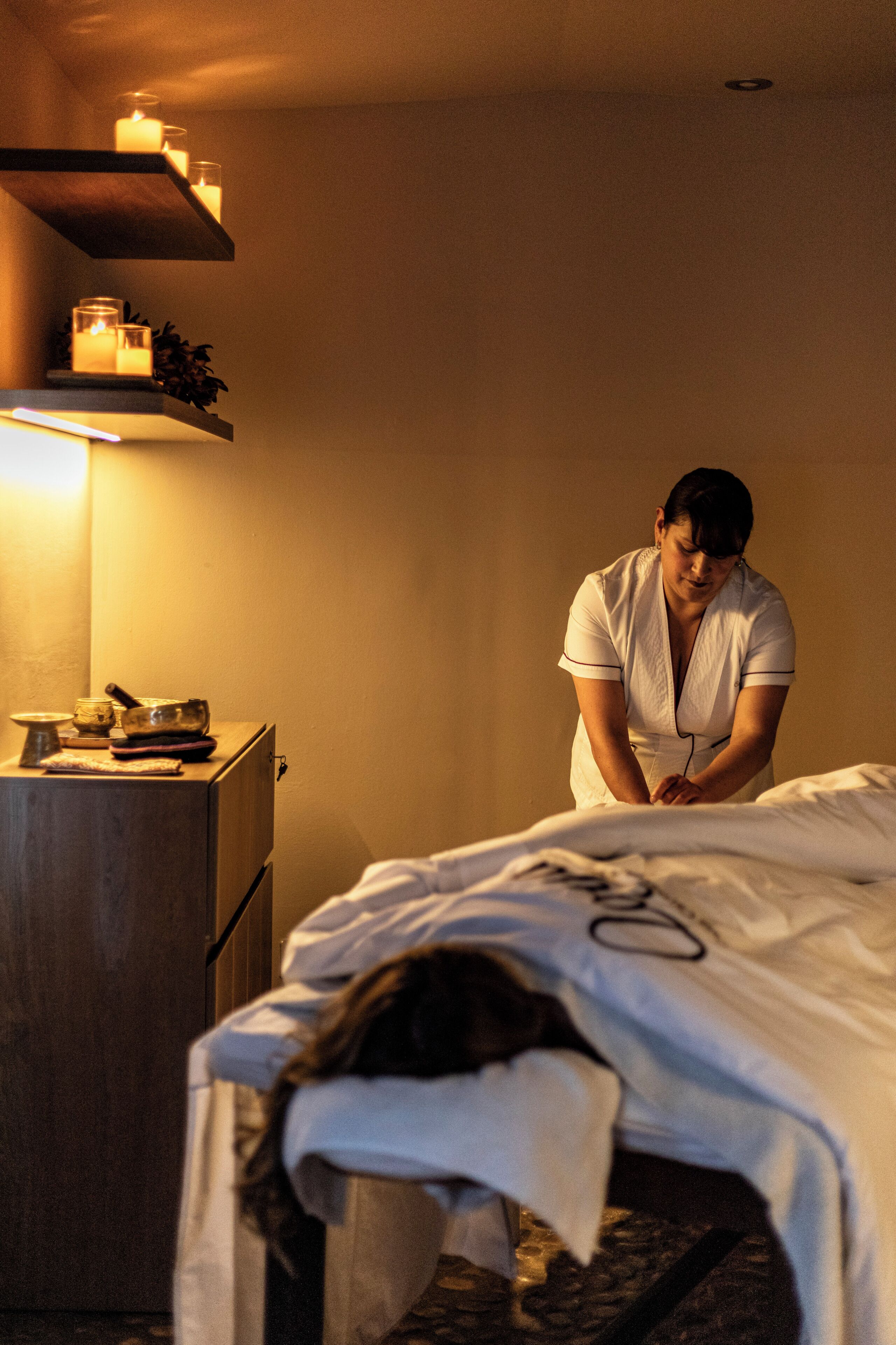 Una habitación de hotel con cama, mesita de noche y estante con velas.
