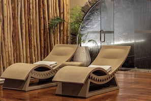 Two lounge chairs with towels, a wooden wall, a plant, and a glass shower enclosure.