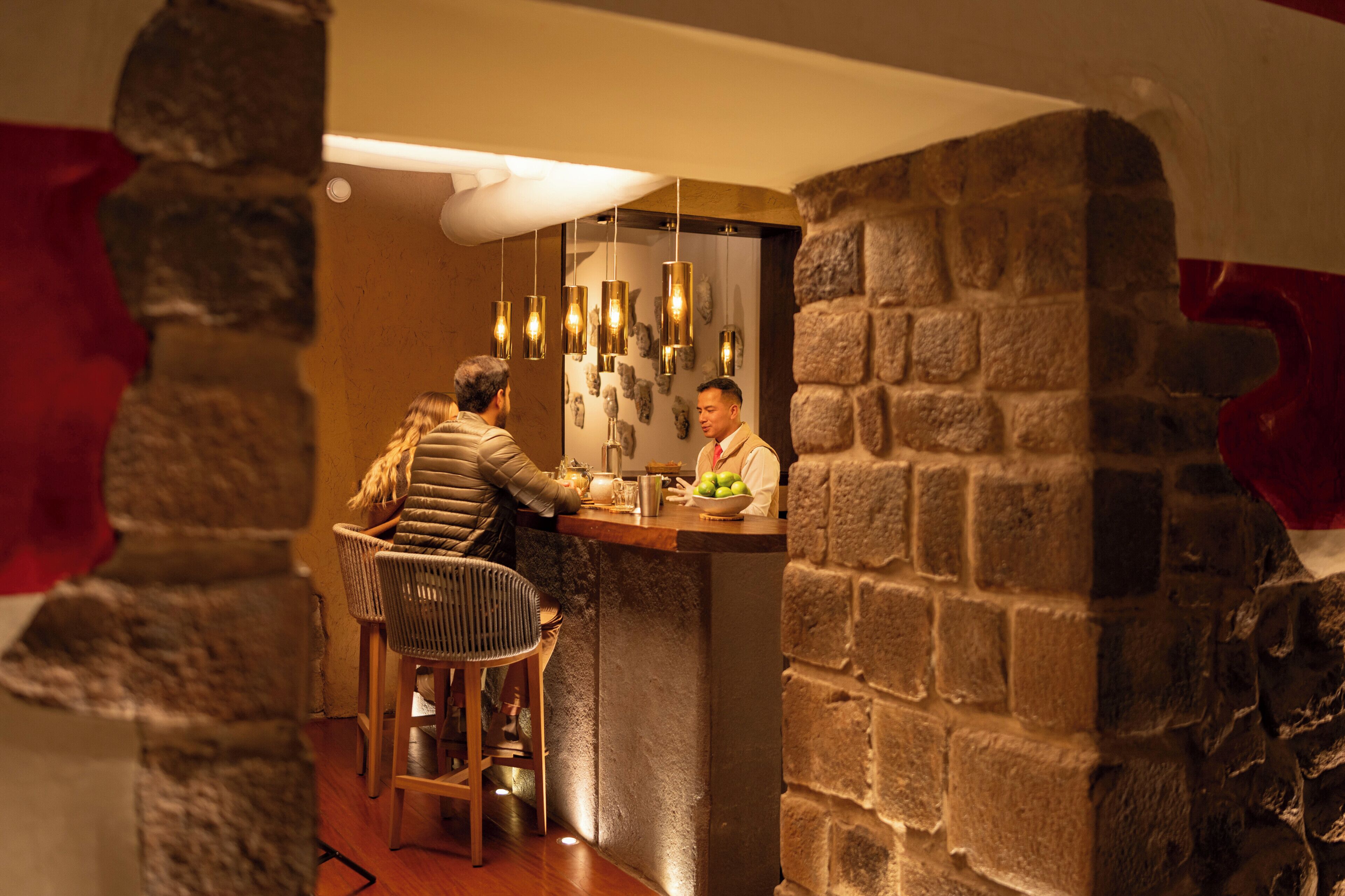 Una zona de bar con pared de piedra, lámparas colgantes y una barra.