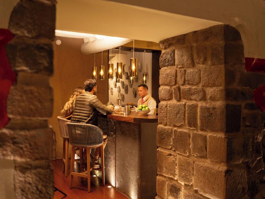 Una zona de bar con pared de piedra, lámparas colgantes y una barra.