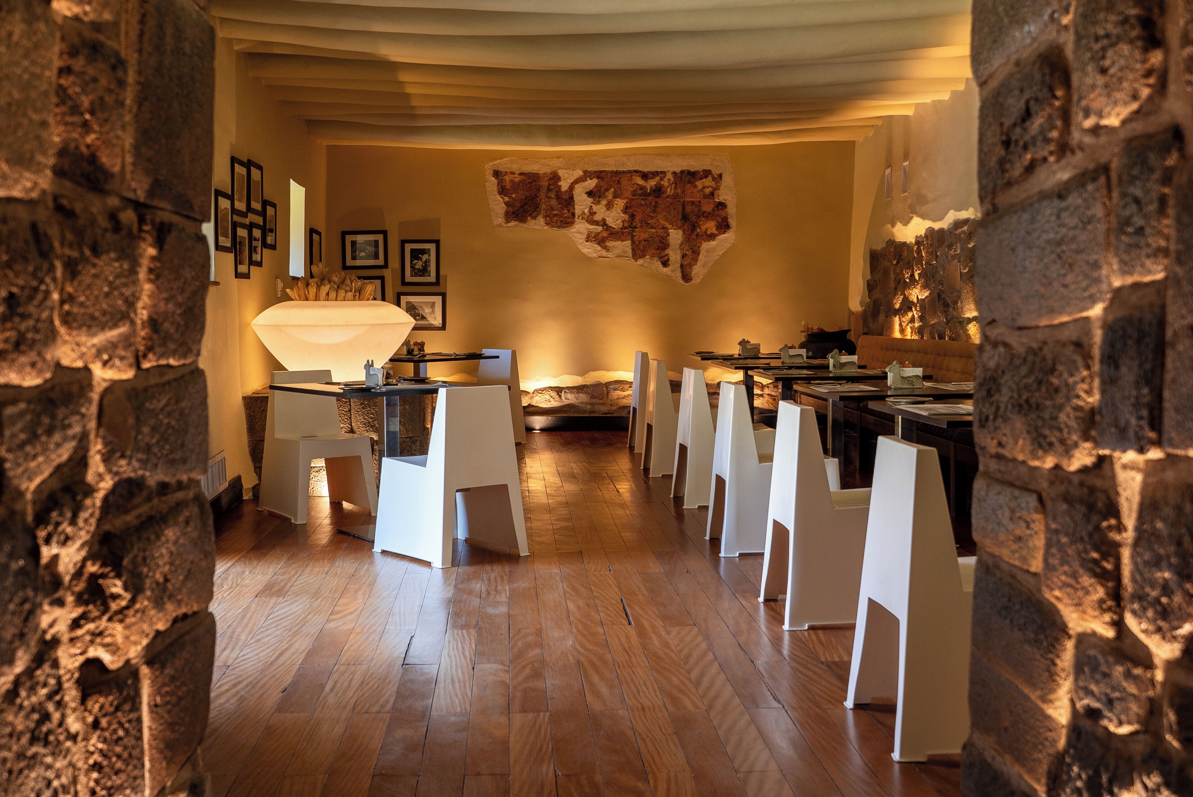 Una habitación con piso de madera, sillas blancas, una mesa y un mapa en la pared.