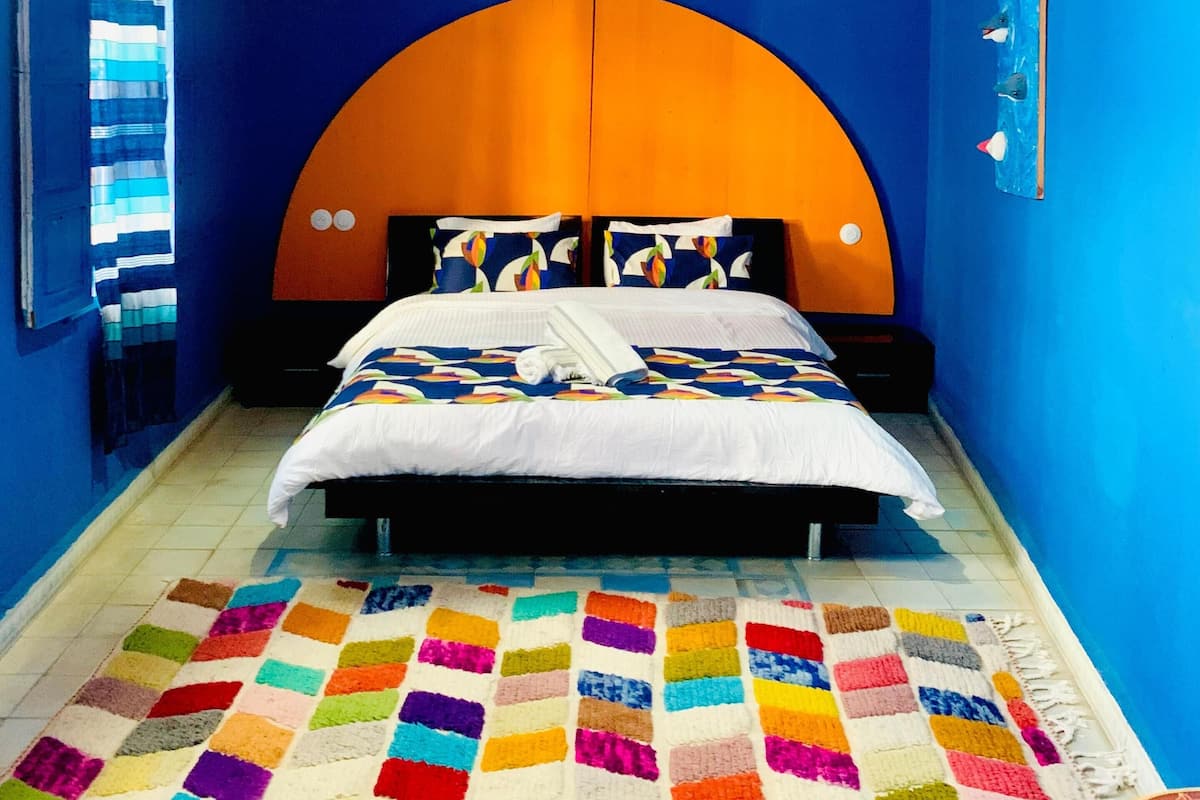 Un dormitorio con una cama, un tapete colorido y una combinación de colores únicos en naranja y azul.
