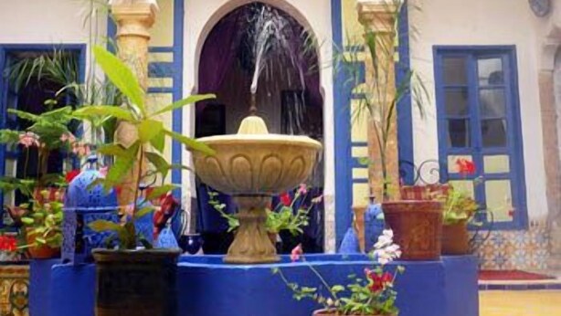A courtyard with a central fountain, surrounded by arches and potted plants.