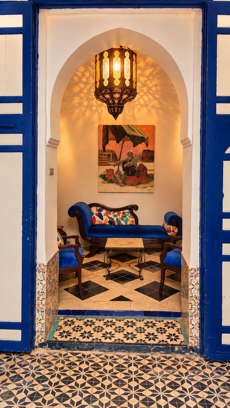 Una habitación con puerta azul, un sofá con cojines de colores, piso estampado y una lámpara colgante.