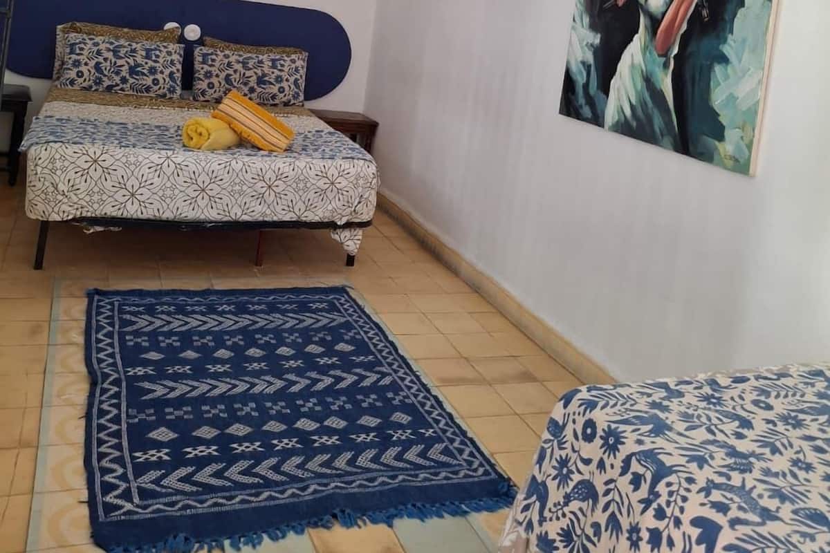 Un dormitorio con cama, un tapete azul estampado, un cuadro en la pared y una lámpara colgante.