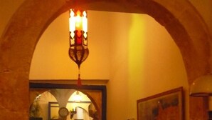 An arched hallway with a chandelier, a painting, and a staircase leading to another room.