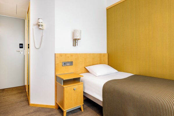 A hotel room with a wooden headboard, a bed with white bedding, a small wooden nightstand, a hairdryer, and a wall-mounted phone.