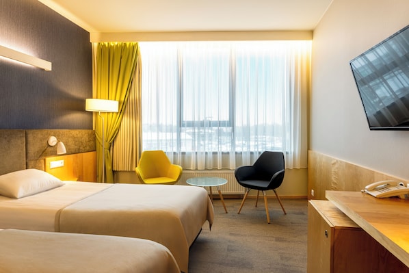 A hotel room with two beds, a desk with a telephone, a chair, a small table, and a TV mounted on the wall. - Tartu Hotel (Tartu)