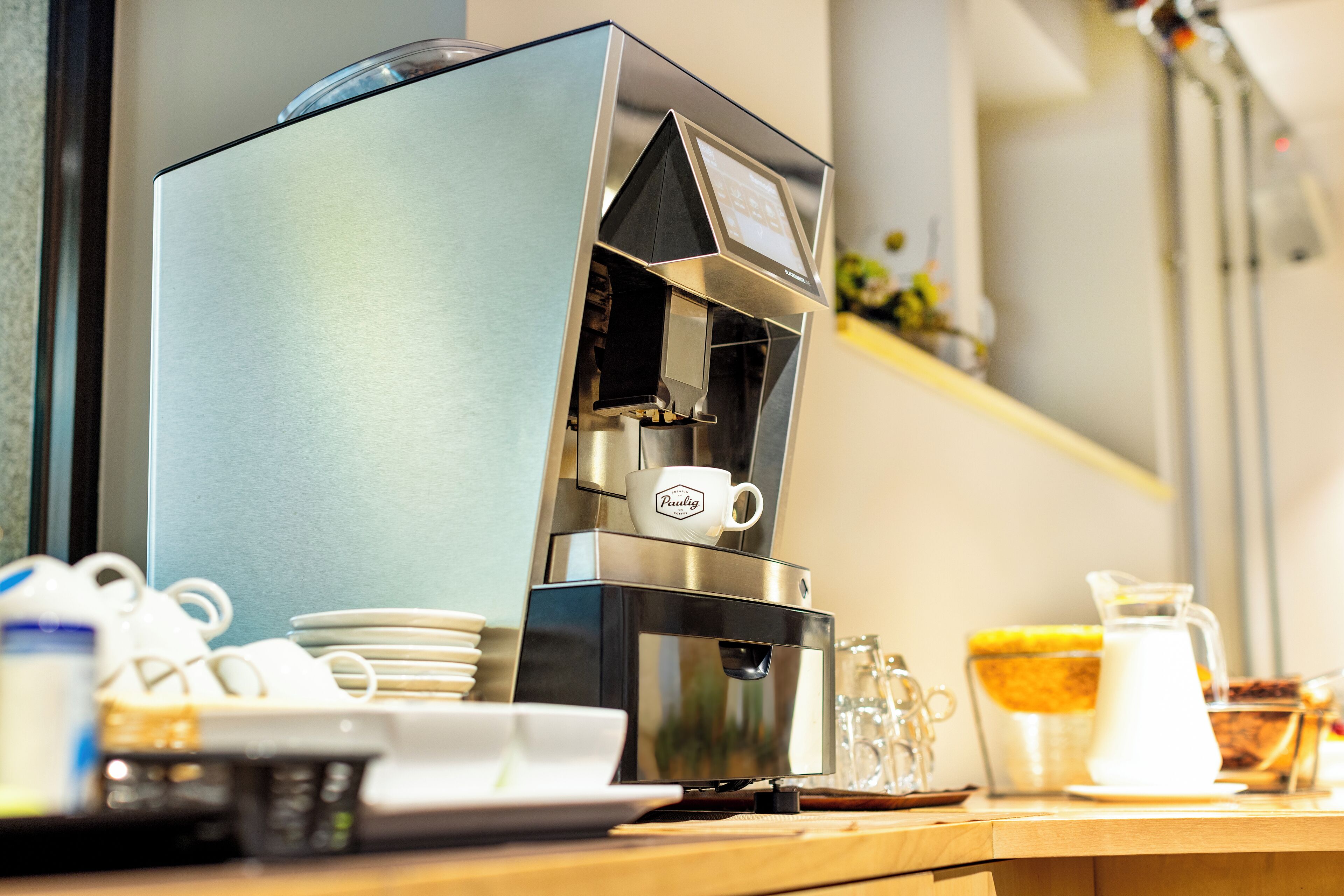 En kaffemaskine med mælkeskummer, en kaffepande og et mælekander på en bordplade.