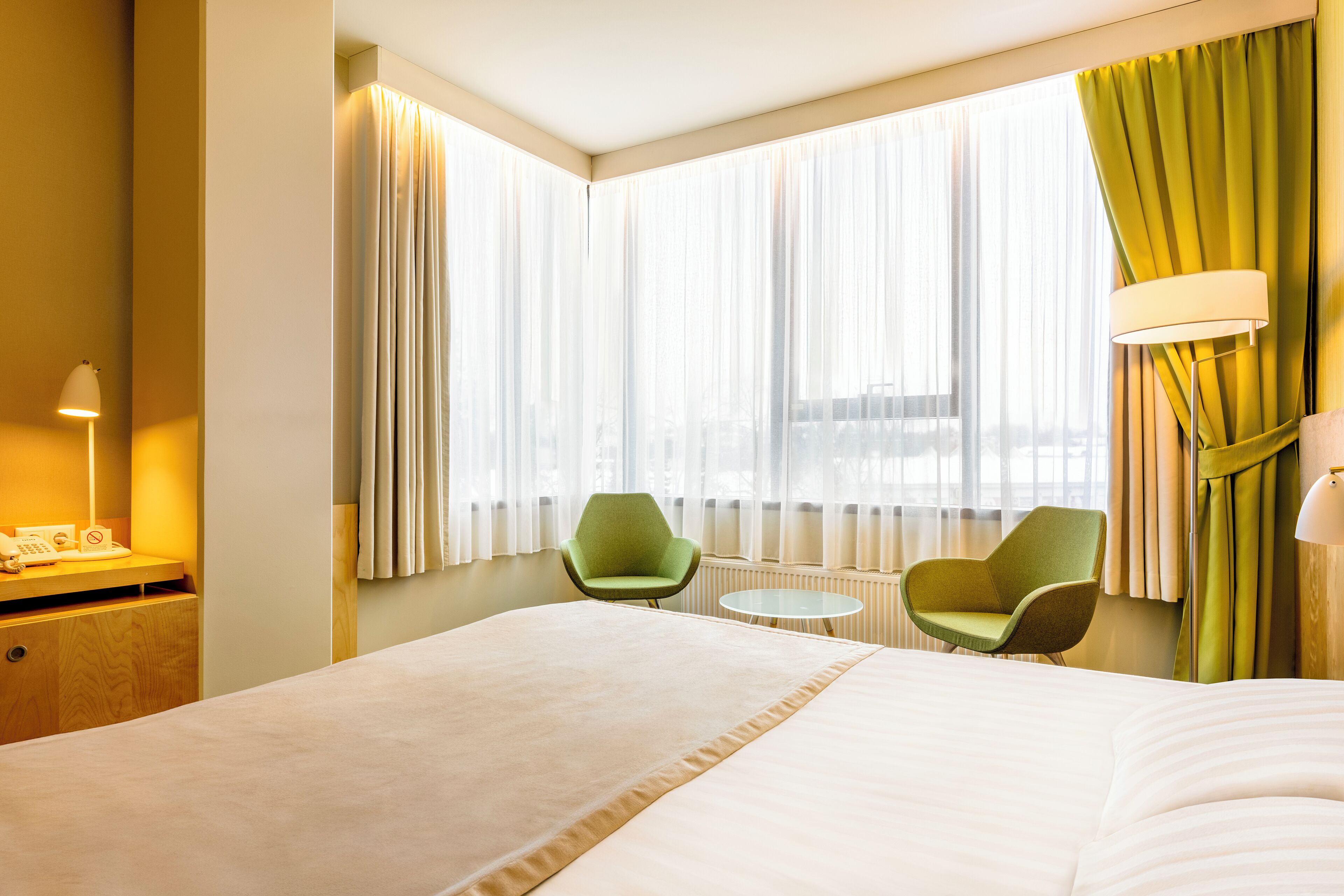 Una habitación de hotel con una cama grande, dos sillas, una mesita y una lámpara.