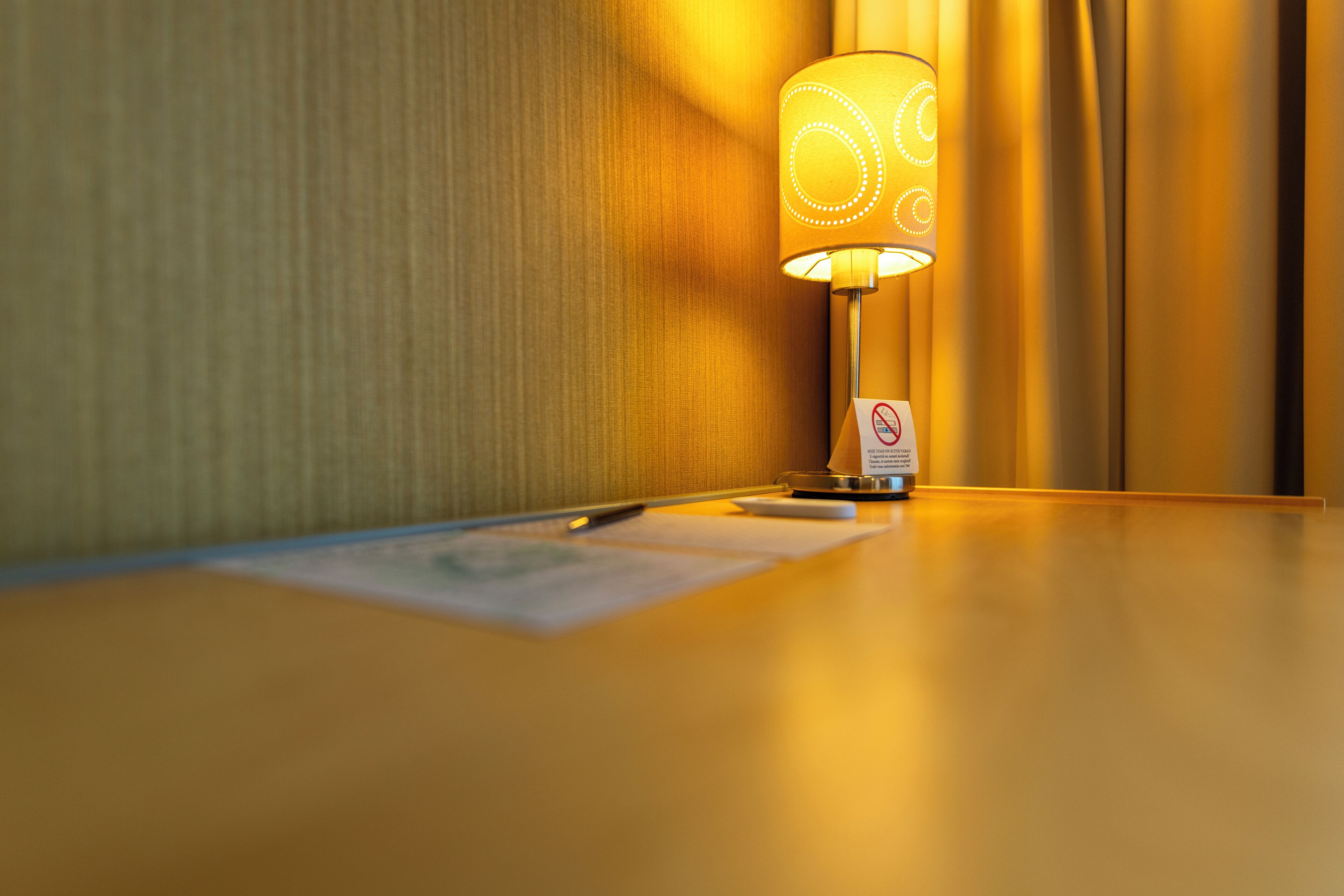 Una habitación de hotel con una lámpara sobre una mesa de madera, un bloc de notas y un bolígrafo.