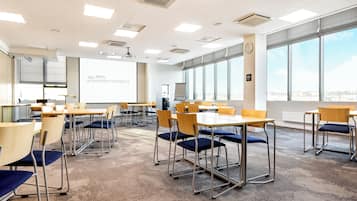 Ein Konferenzraum mit Tischen, Stühlen, großen Fenstern und einer Projektionsleinwand.