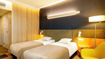 A hotel room with two beds, a wooden slat wall, a modern lamp, and a yellow chair.